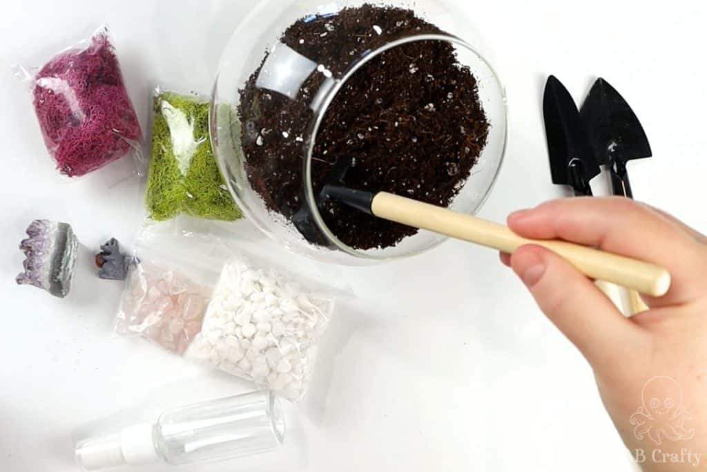 using a small rake to even out the dirt in the glass container