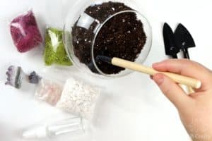 using a small rake to even out the dirt in the glass container