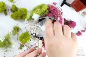 pouring pebbles over the dirt in the glass container in front of the moss