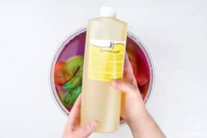 holding a bottle of jacquard synthrapol over a bowl with dyed wool in water