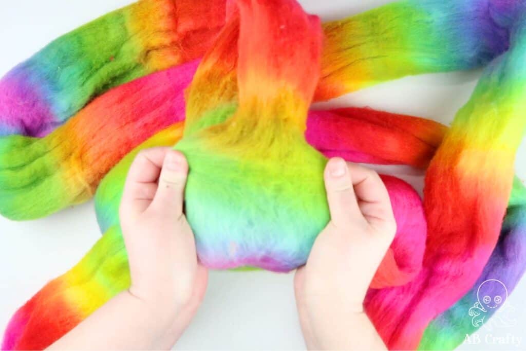 using two hands to hold either side of rainbow dyed wool roving to separate the fibers