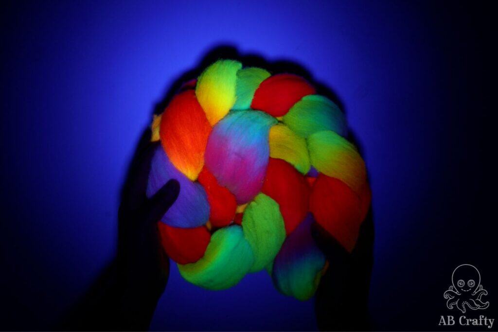 holding rainbow dyed wool under a blacklight to show how it glows different colors in a blacklight