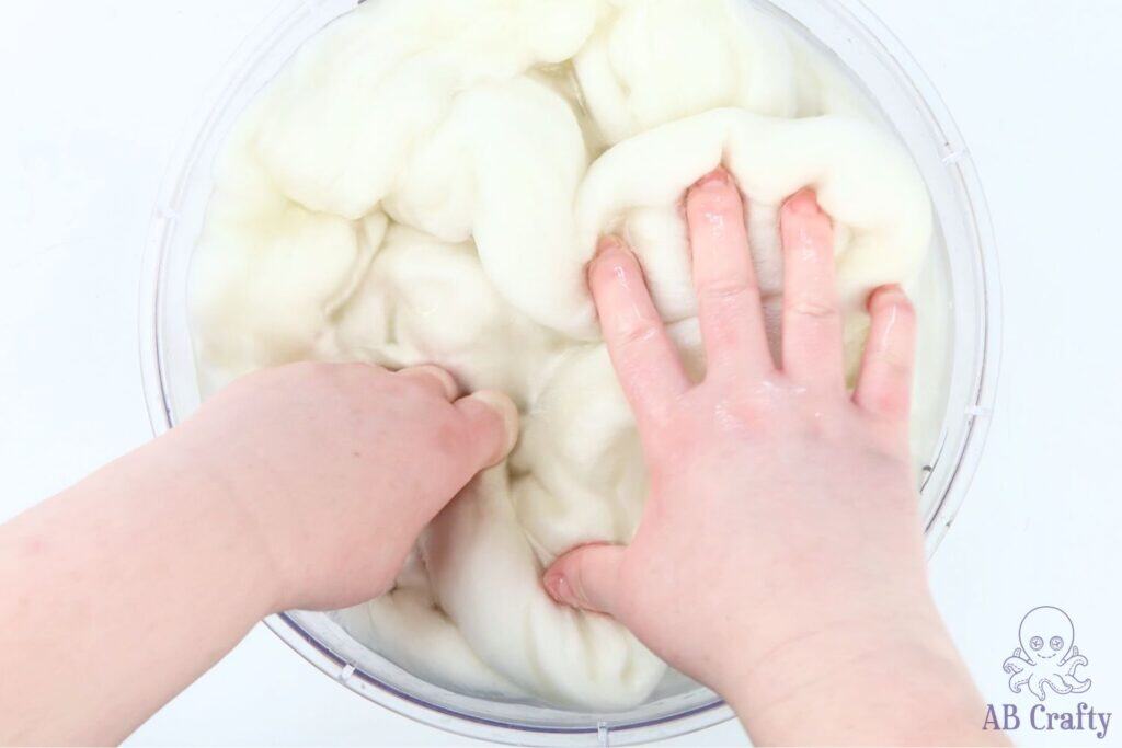 hands pushing undyed wool roving into a bowl of water and vinegar
