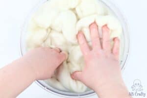 hands pushing undyed wool roving into a bowl of water and vinegar