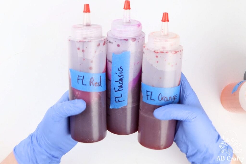 hands in nitrile gloves holding 3 dye bottles with blue tape labels