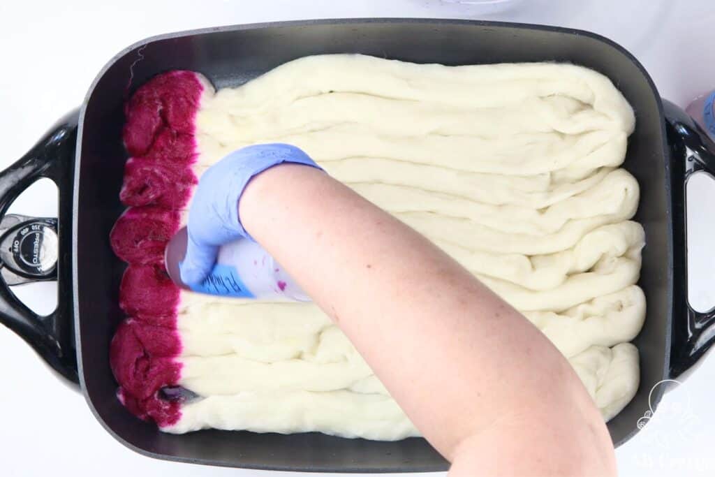 using a bottle to squeeze pink dye onto undyed wool in an electric skillet