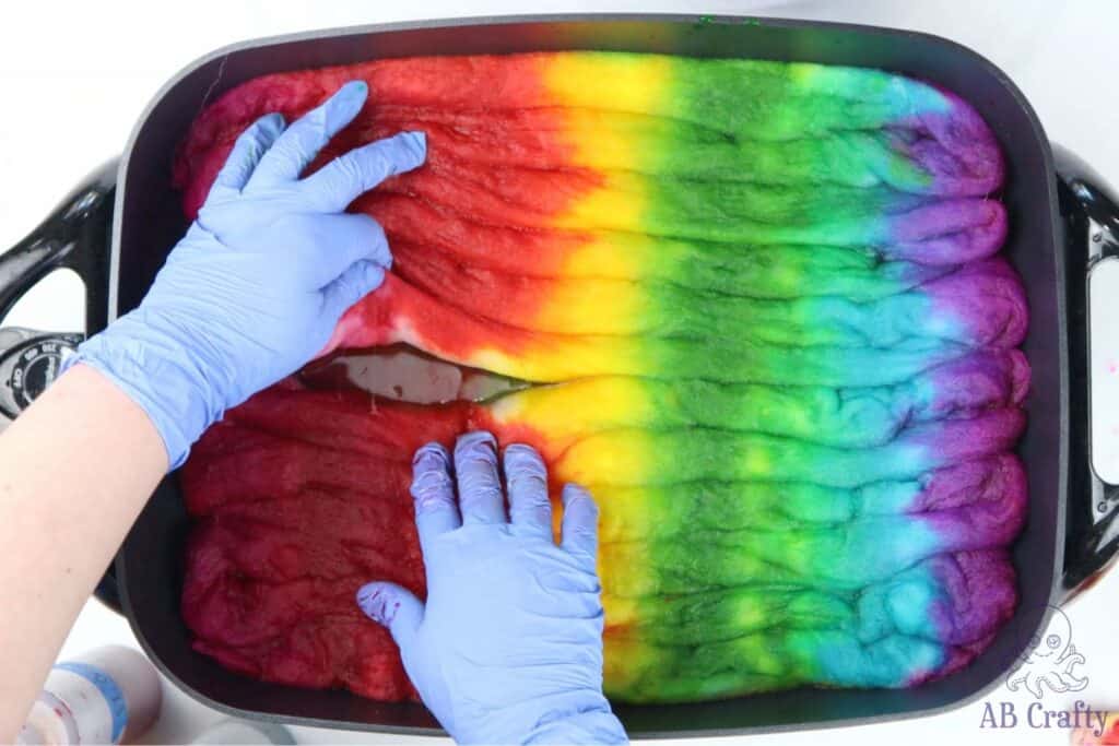 using hands wearing nitrile gloves to separate rows of dyed wool that are dyed in a rainbow stripe pattern