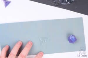 purple resin die on top of some sand paper with water on it with a d4 in the corner