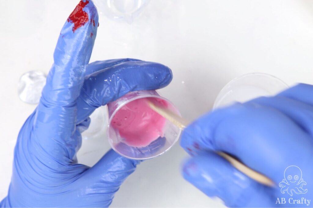putting a popsicle stick into some liquid silicone that has been dyed pink with silicone pigment