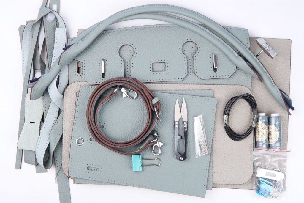all of the materials from the babylon leather birkin bag kit in haze blue laid out on a white table. includes pre-cut leather purse pieces